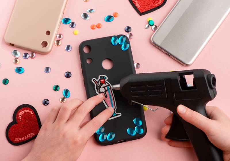 Fille attachant un patch de cocktail sur un étui de téléphone noir avec un pistolet à colle | Etuis de téléphone