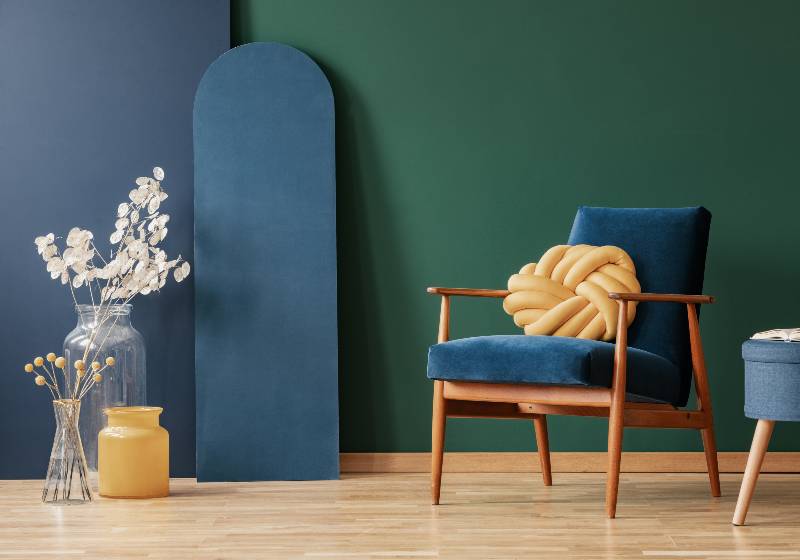 Oreiller jaune sur un fauteuil en bois dans un intérieur plat bleu et vert avec des fleurs et un tabouret | Knot Pillow